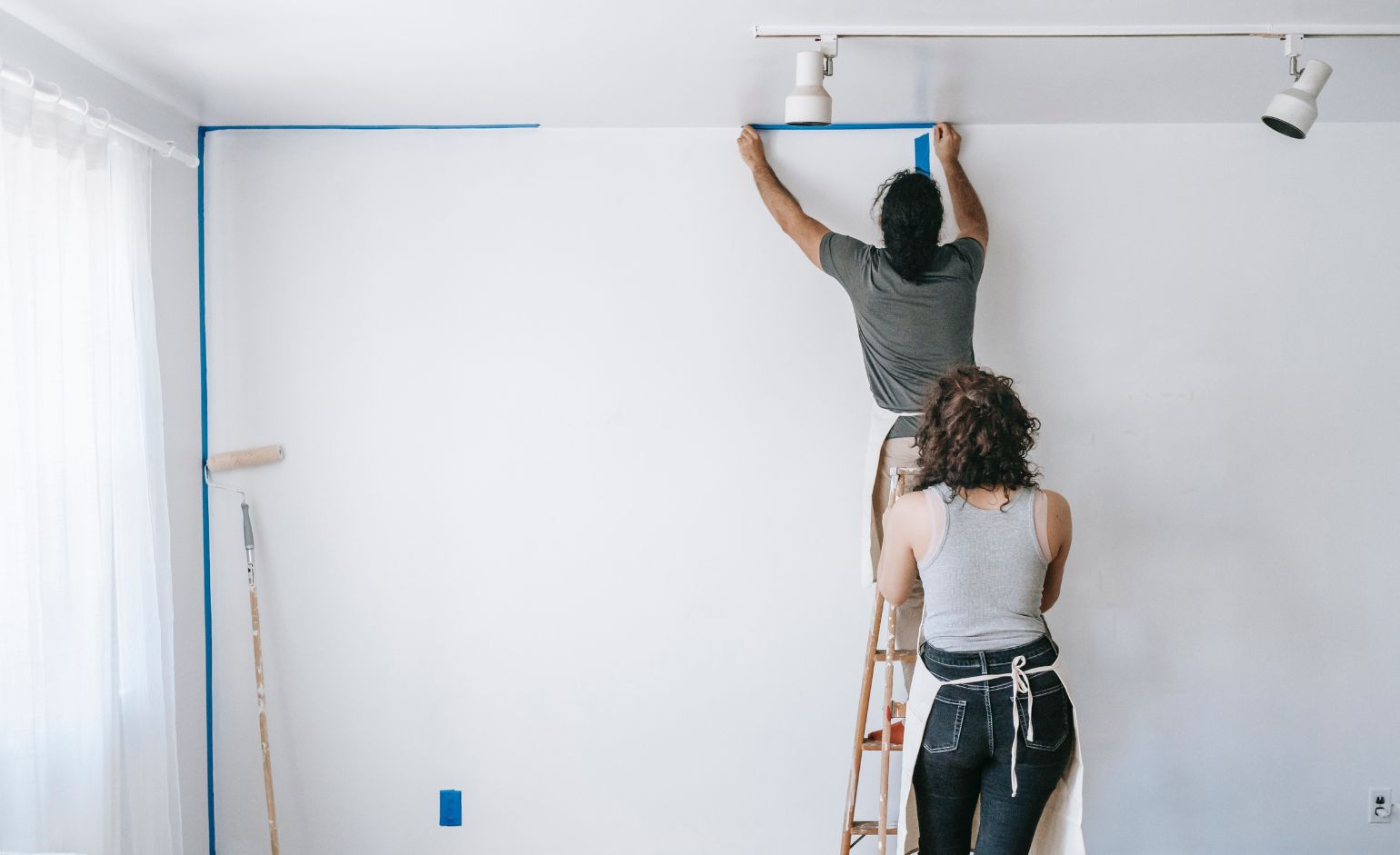 Man putting blue tape on wall to prepare for painting